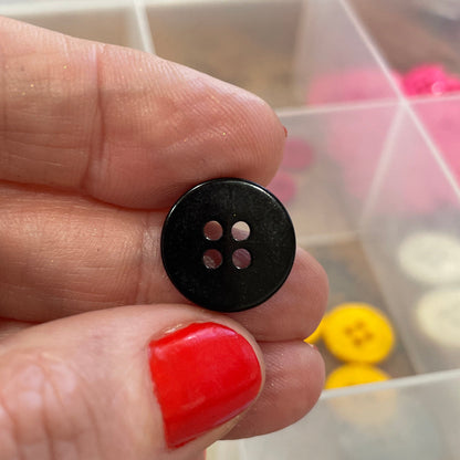 Hand holding a black button with a container of colorful buttons in the background