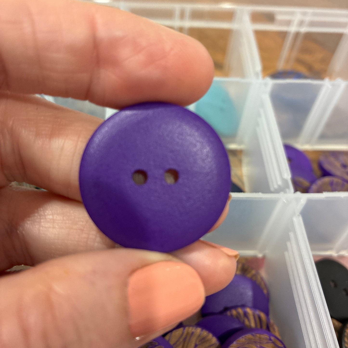 Hand holding a purple button with a container of buttons in the background