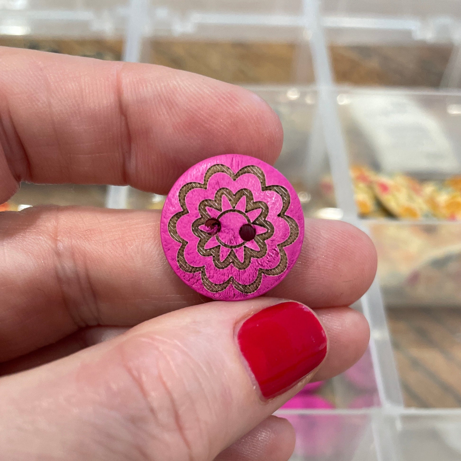 Hand holding a pink button with floral design in front of a display case with various buttons.
