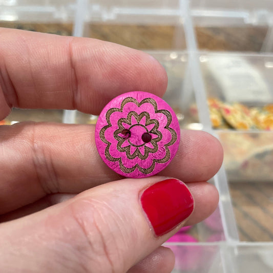 Hand holding a pink button with floral design in front of a display case with various buttons.