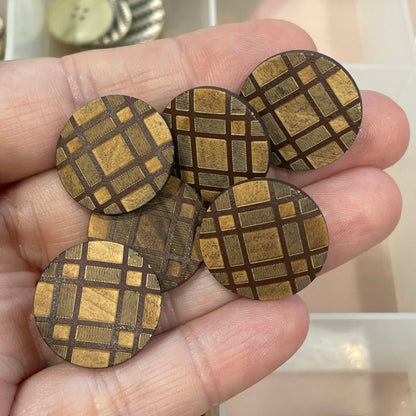 Hand holding decorative buttons with a clear container of various buttons in the background