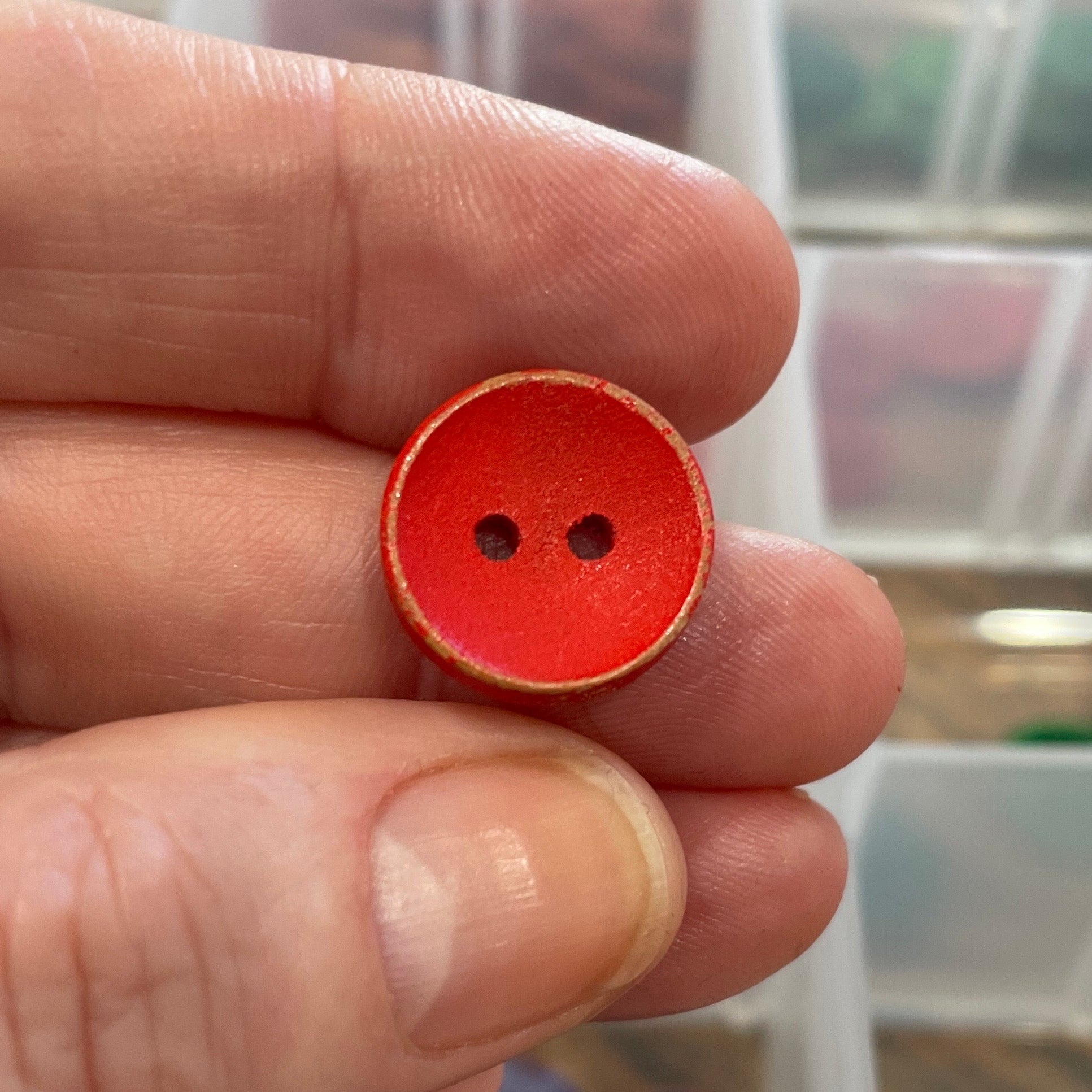 Hand holding a red button with a clear container of buttons in the background