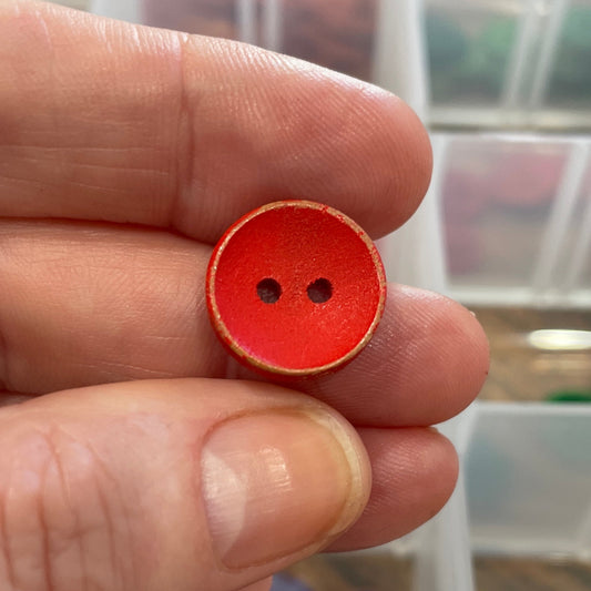 Hand holding a red button with a clear container of buttons in the background