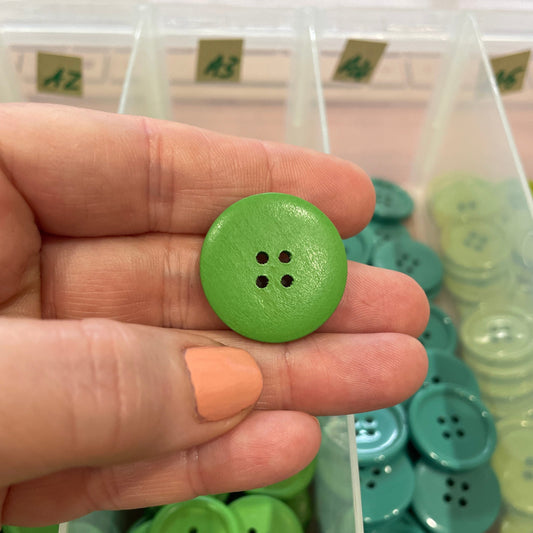 Green button held between fingers with a container of green buttons in the background