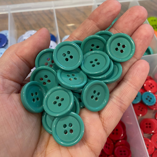 Hand holding green buttons with a container of red buttons in the background