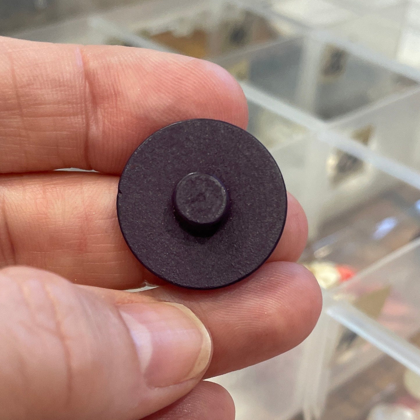 Hand holding a button with a clear container of assorted items in the background