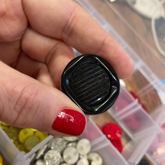 Hand holding a black object with a textured surface, surrounded by various colored buttons in the background.