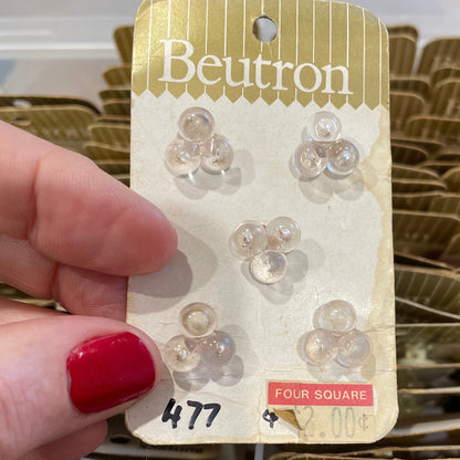 Hand holding a Beutron button package with multiple packages in the background.