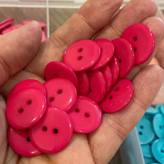Hand holding pink buttons with a container of blue and red buttons in the background