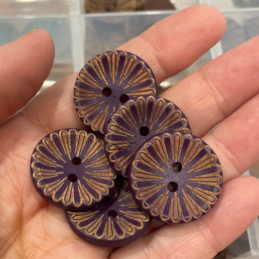 Hand holding four decorative buttons with a clear container of buttons in the background