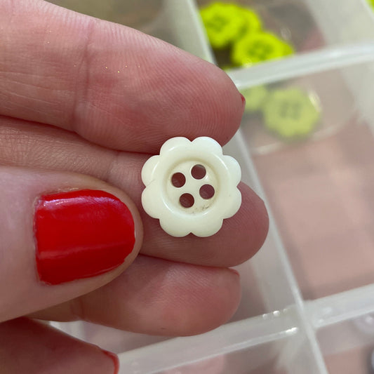 Hand holding a white button with a clear container of buttons in the background