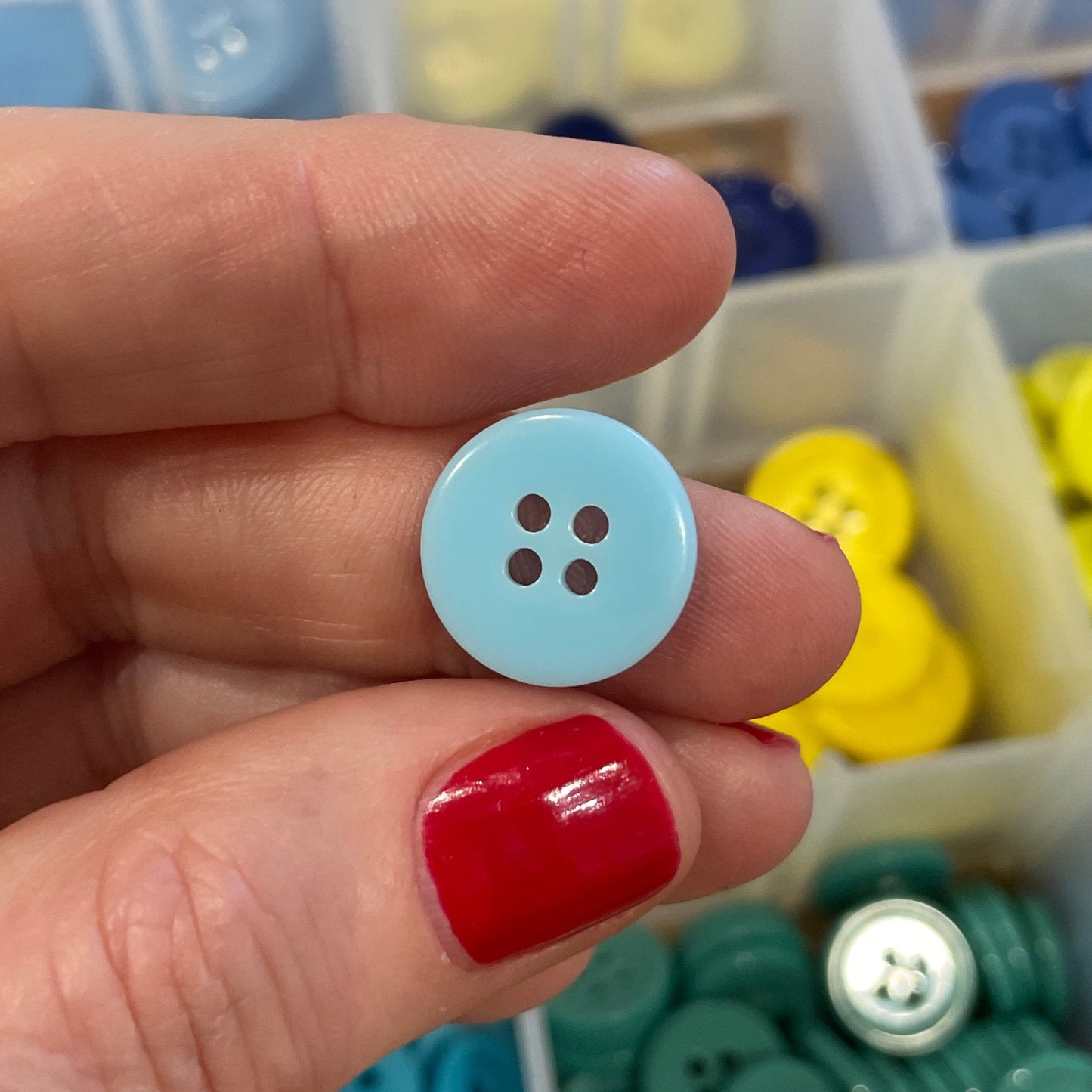 Hand holding a blue button with a container of colorful buttons in the background