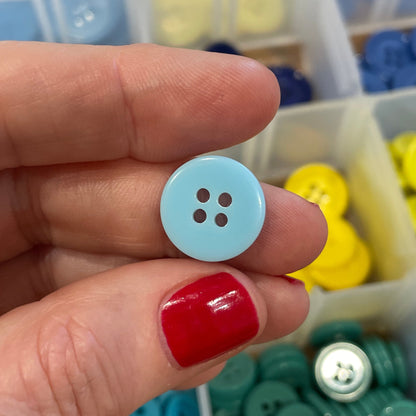 Hand holding a blue button with a container of colorful buttons in the background