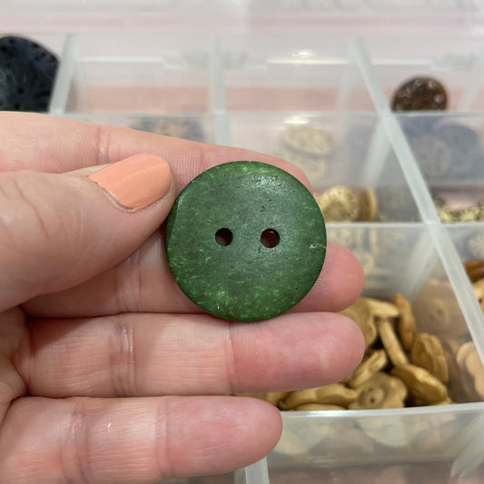 Hand holding a green button with a container of buttons in the background