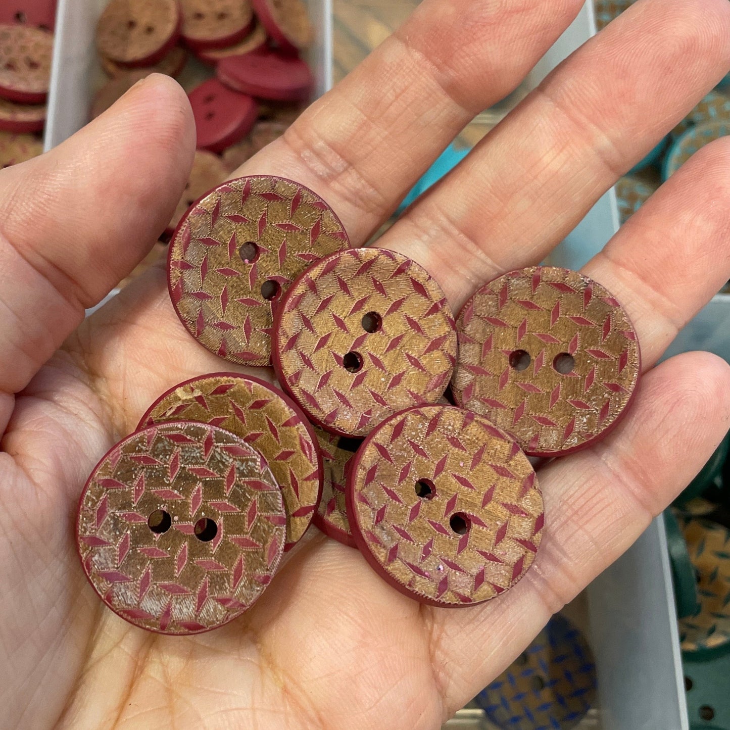Hand holding wooden buttons with a clear container of buttons in the background