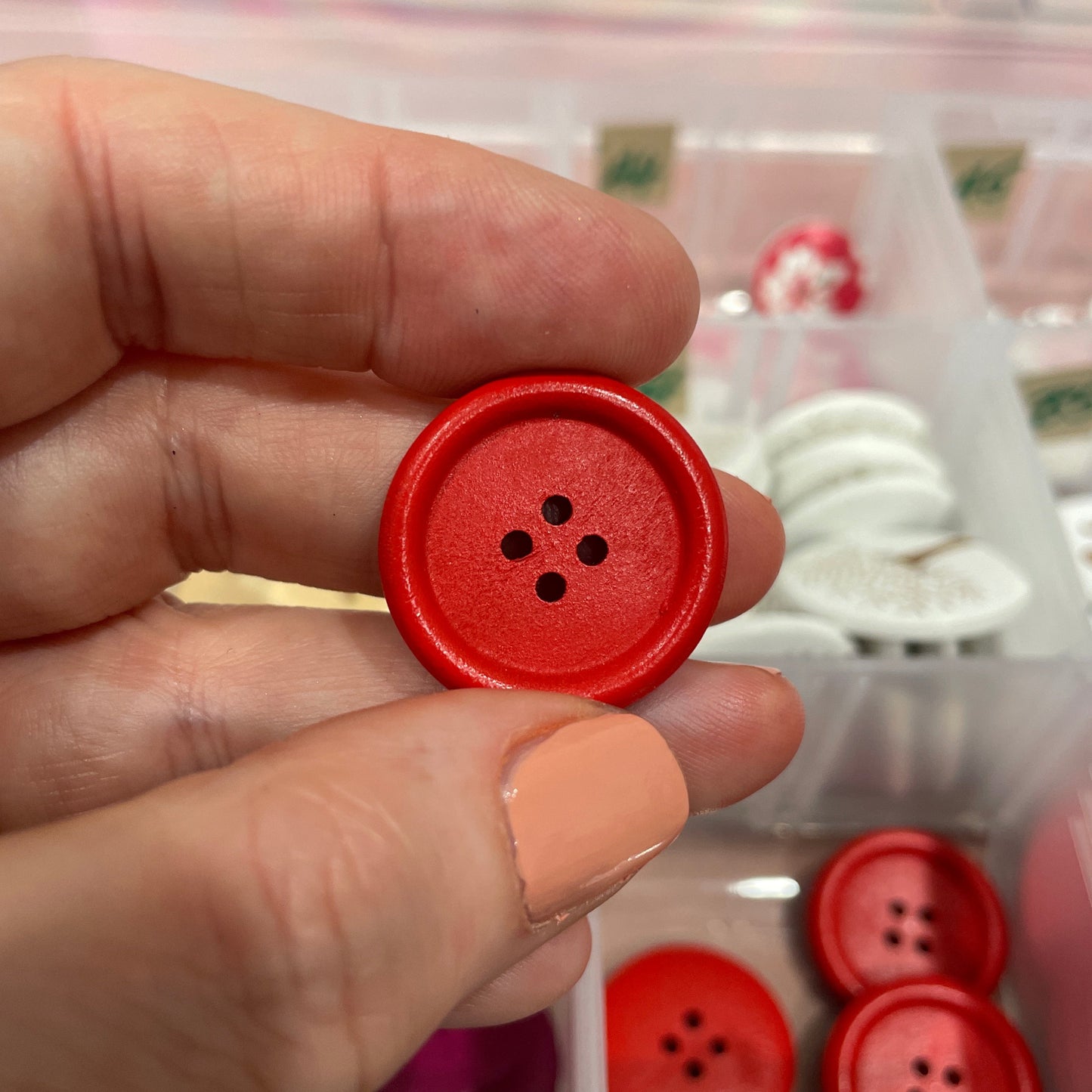 Red button held by a hand with a background of more buttons in a case.