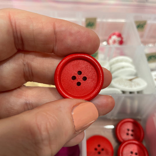 Red button held by a hand with a background of more buttons in a case.
