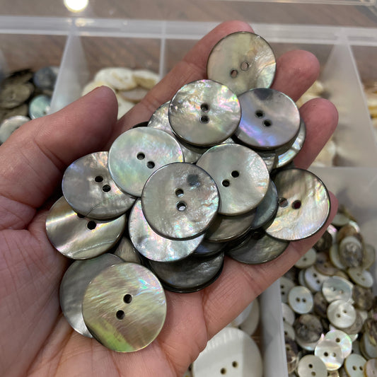 Hand holding a collection of shell buttons with a blurred background of more buttons.
