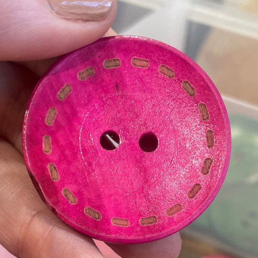 Pink button with cut-out design held by a hand, with more pink buttons in the background.