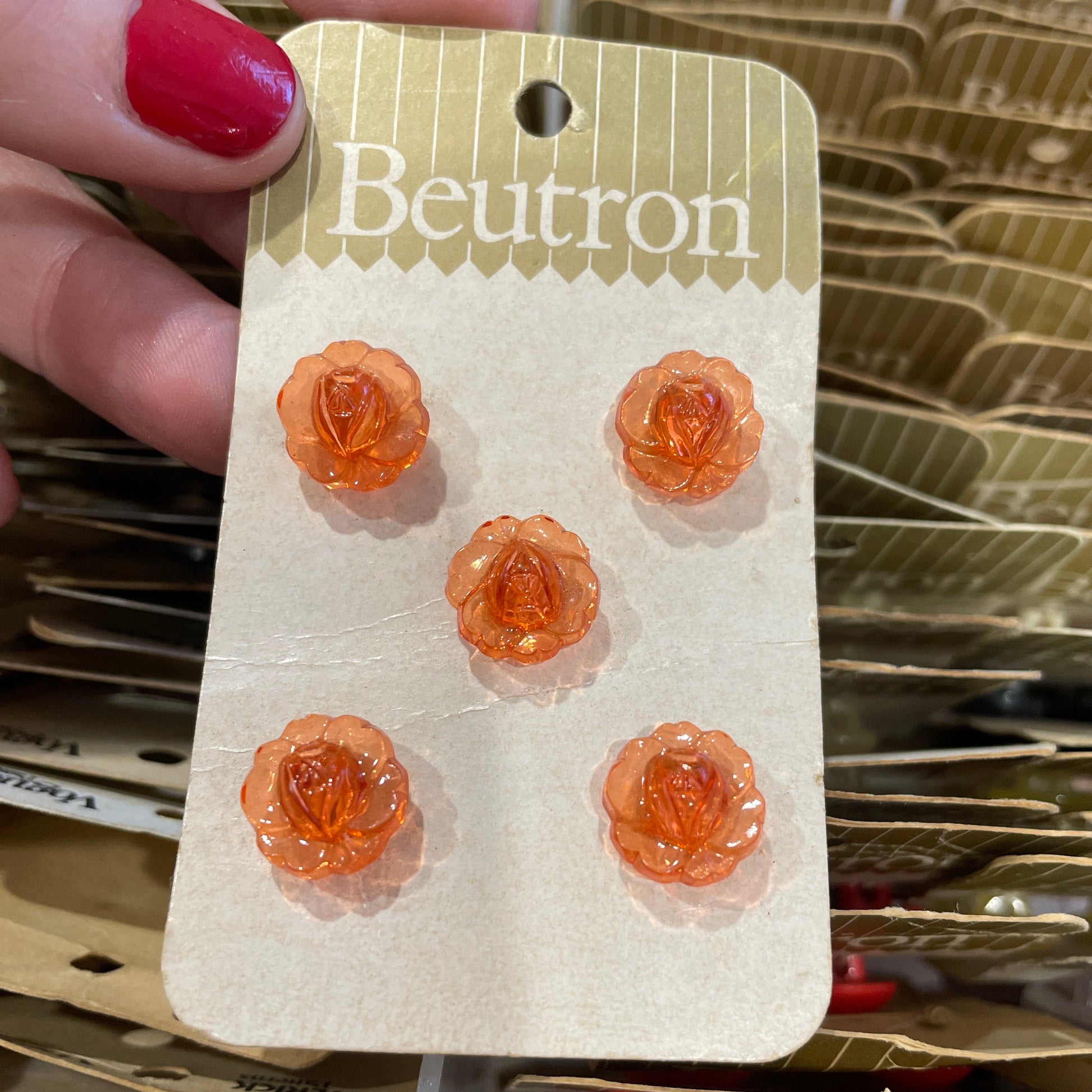 Set of orange rose-shaped buttons on a card held by a hand with red nail polish.