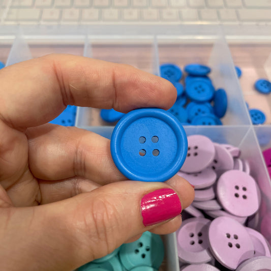 Hand holding a blue button with a container of colorful buttons in the background
