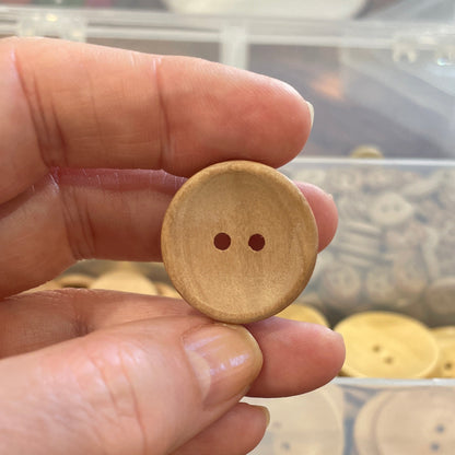 Hand holding a wooden button with a blurred background of assorted buttons