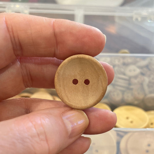 Hand holding a wooden button with a blurred background of assorted buttons
