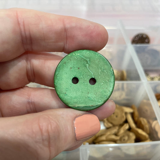 Green button held by a hand with a clear container of buttons in the background
