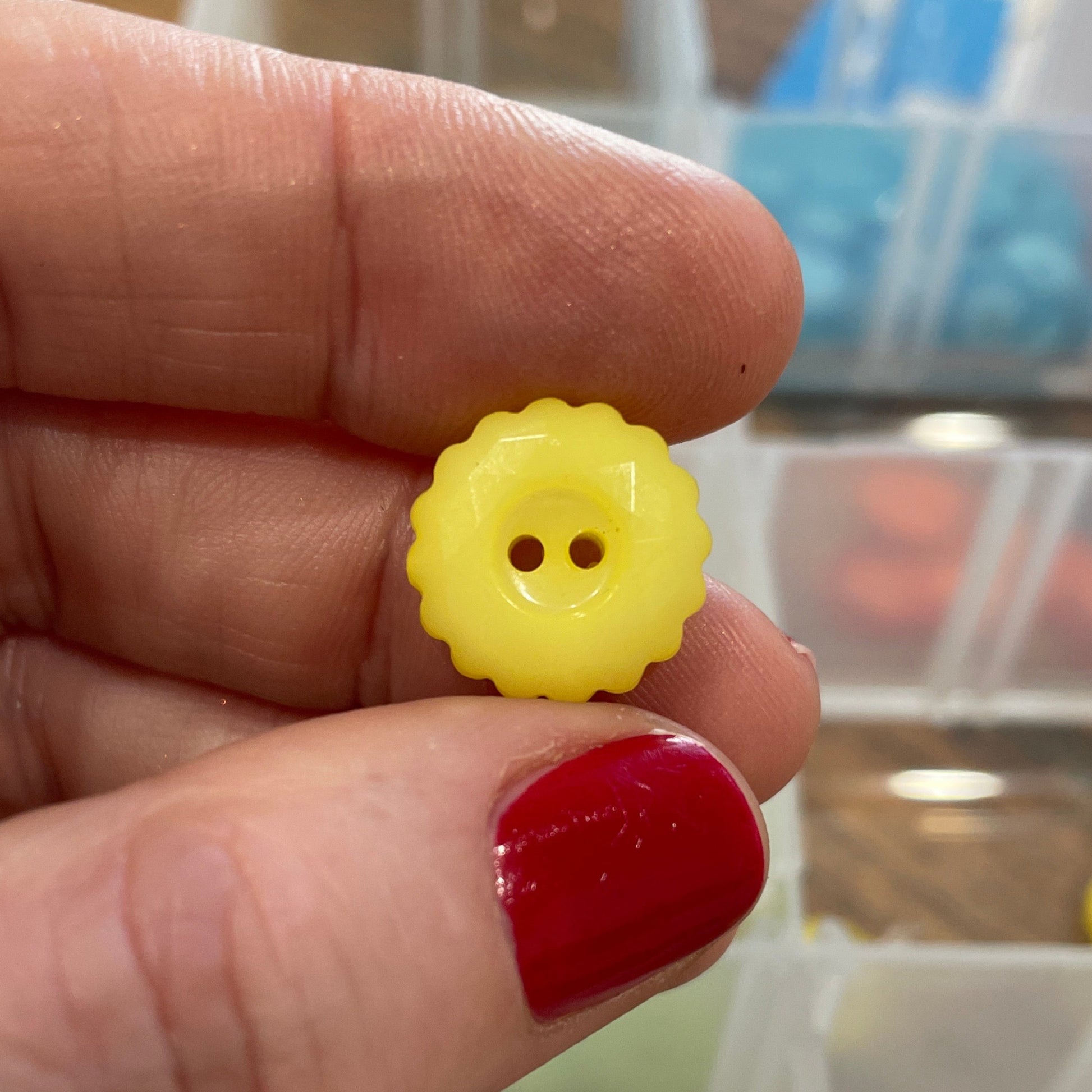 Hand holding a yellow button with a blurred background of button collection