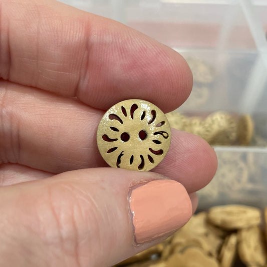 Hand holding a gold button with a container of buttons in the background