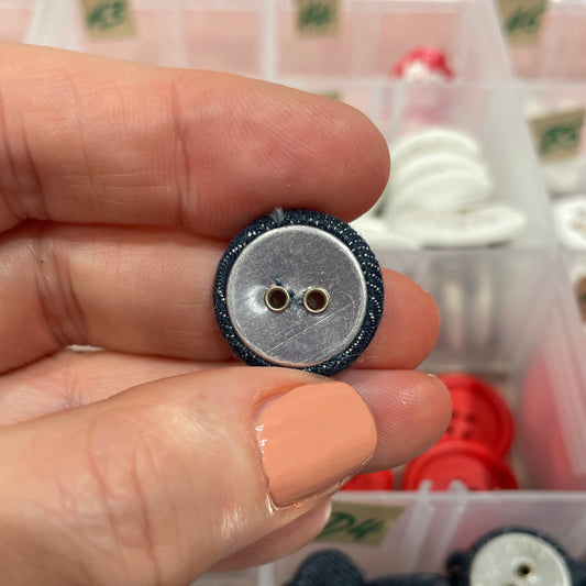 Hand holding a button with a background of various buttons in containers