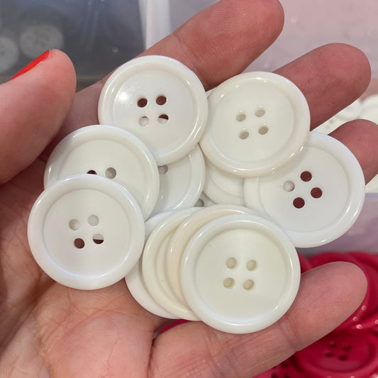 Hand holding white buttons with a container of red and black buttons in the background