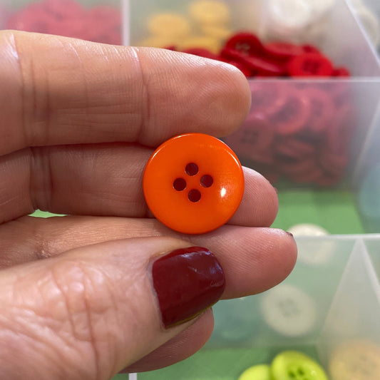 Hand holding an orange button with a clear container of buttons in the background