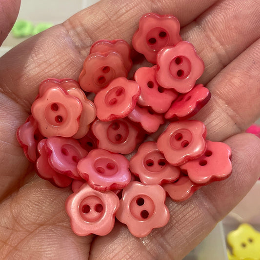 Hand holding pink flower-shaped buttons with a blurred background of more buttons.