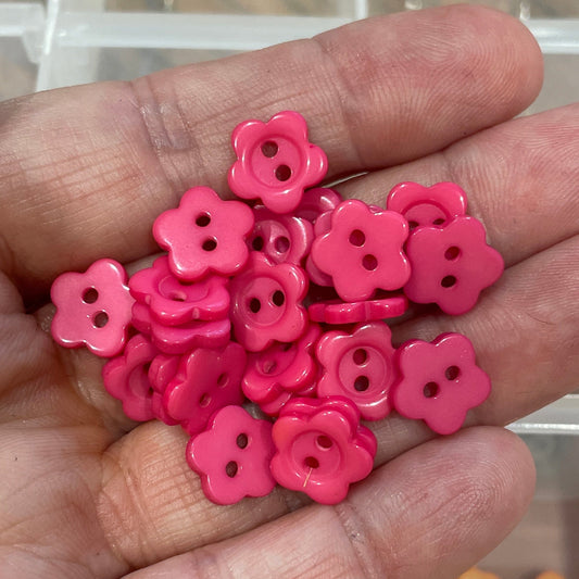Hand holding pink flower-shaped objects with a clear container of assorted small items in the background.