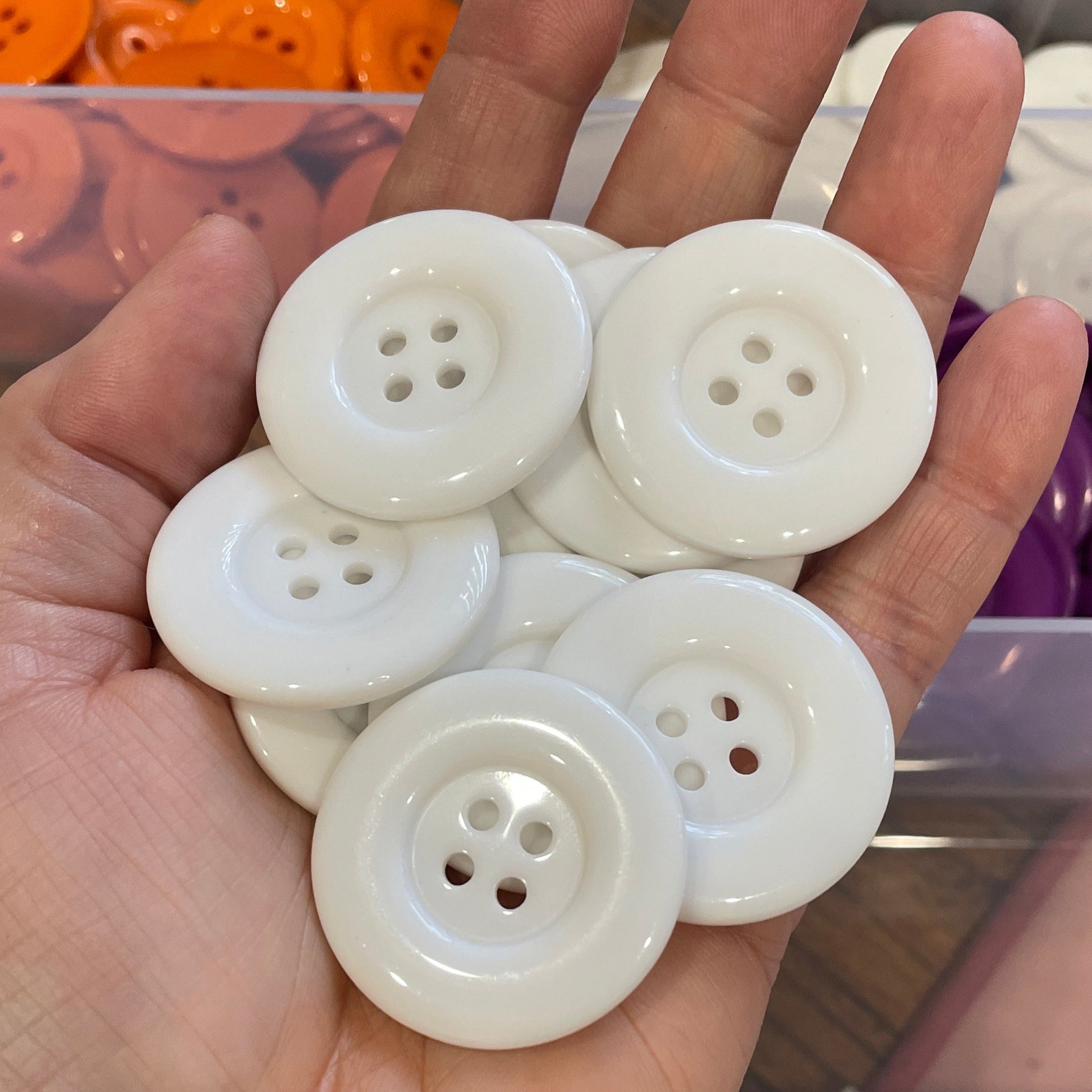 Hand holding white buttons with a container of buttons in the background