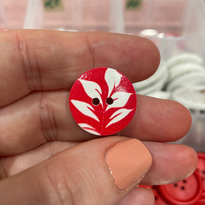 Red and white button held between fingers with blurred container of buttons in the background