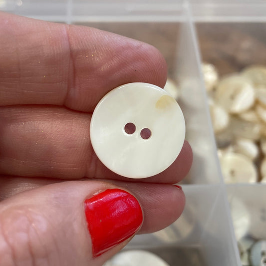White button held between fingers with a container of buttons in the background
