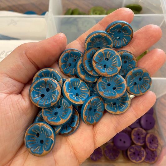 Hand holding blue buttons with a clear container of more buttons in the background.