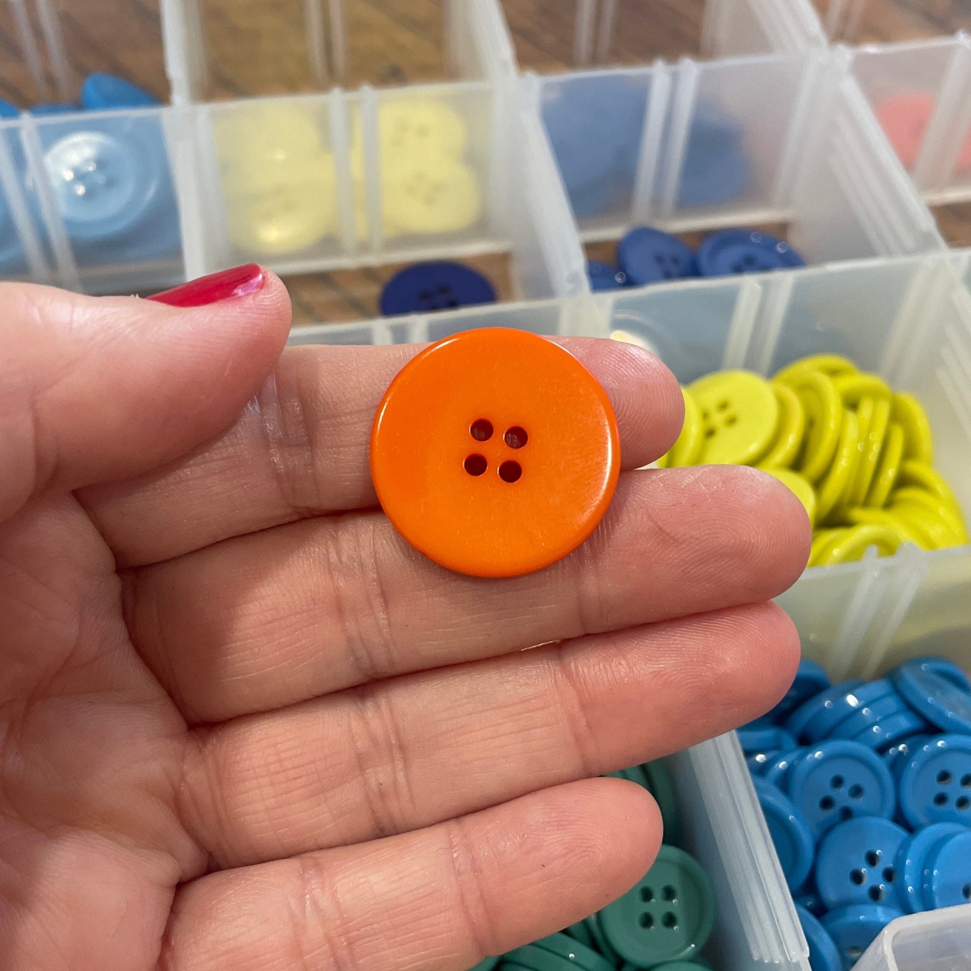 Hand holding an orange button with a container of colorful buttons in the background