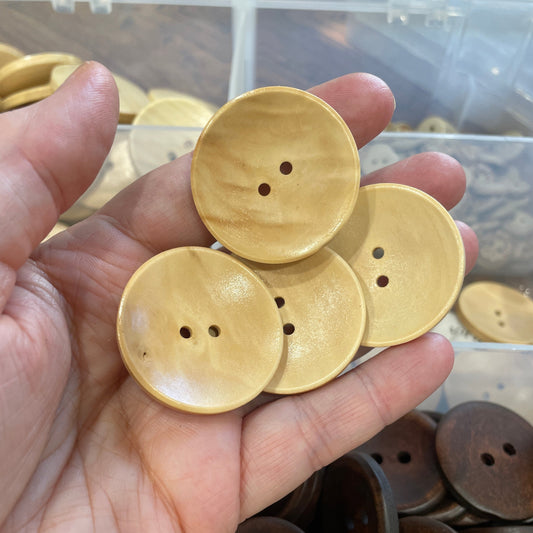 Hand holding buttons with a container of brown buttons in the background