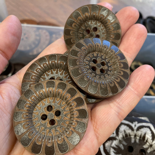 Hand holding three decorative buttons with intricate designs against a blurred background.