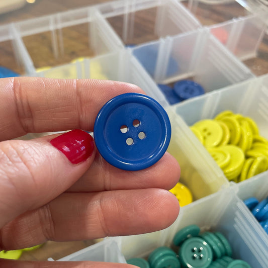 Hand holding a blue button with containers of buttons in the background