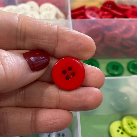 Hand holding a red button with a clear container of assorted buttons in the background