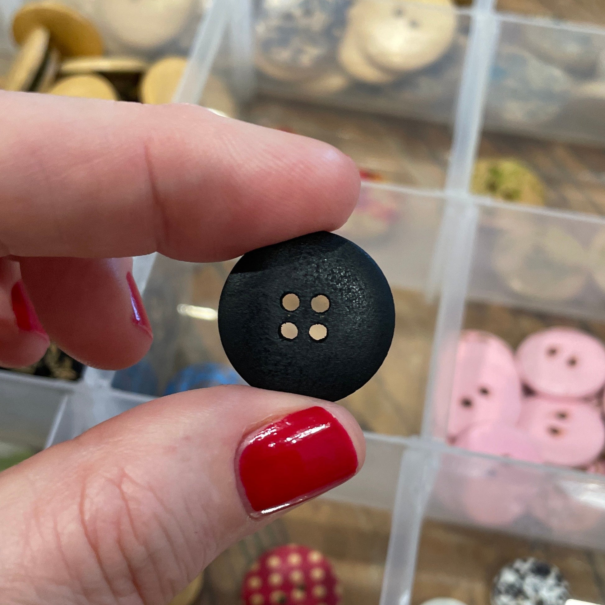 Person holding a black button with a clear container of buttons in the background