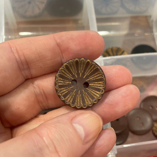 Hand holding a bronze button with a container of various buttons in the background