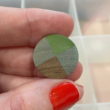 Hand holding a round, multicolored button with a button organizer in the background.