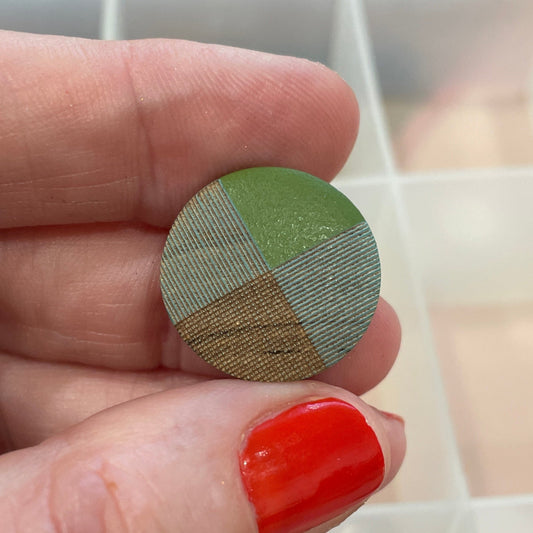 Hand holding a round, multicolored button with a button organizer in the background.