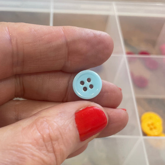 Hand holding a small blue button with a clear container of buttons in the background