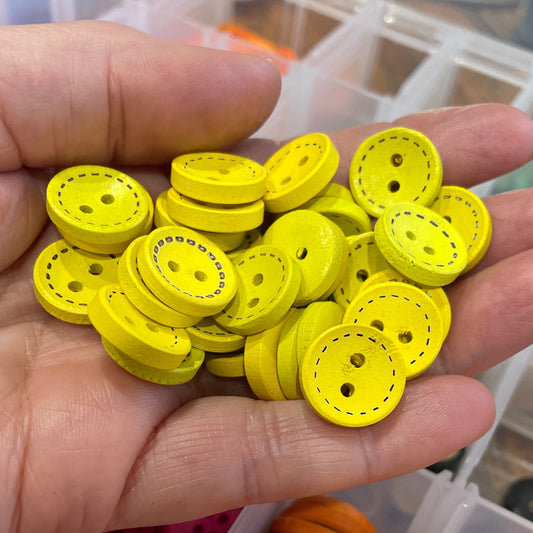 Hand holding yellow buttons with a container of orange buttons in the background